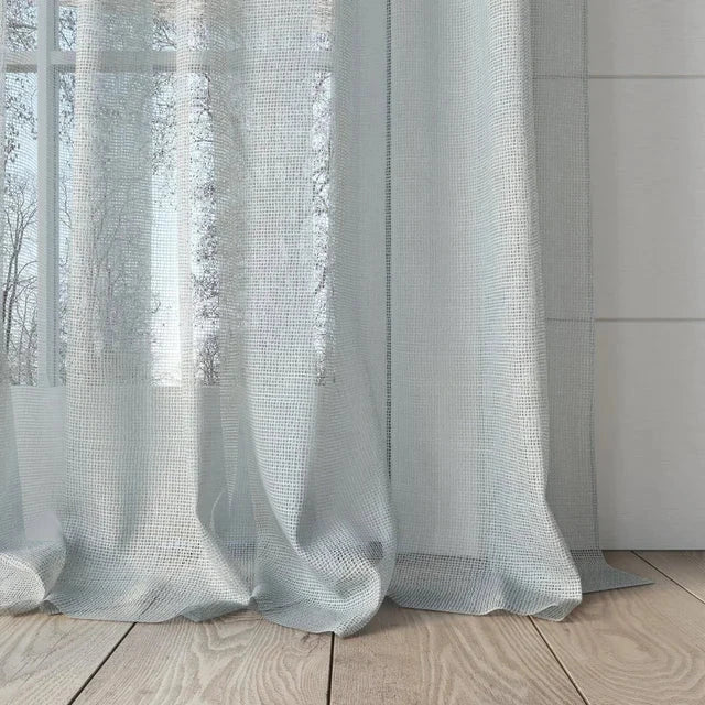 Sheer white curtains with a subtle pattern hanging in front of a window.