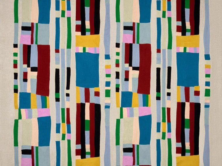 An abstract geometric textile or wall hanging with vertical bands of colored rectangular blocks on a light neutral background. The pattern includes blue, red, green, yellow, pink, black, and cream tones.