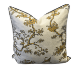 Square decorative throw pillow featuring a gold and brown floral branch pattern on a textured cream background with a dark piped edge.