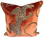 A square velvet throw pillow in a warm rust-orange color, featuring a bold leopard print pattern with black and beige spots.