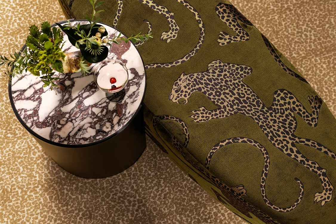 Round marble table with a plant next to a green cushion with animal patterns by Catherine Martin Fabrics