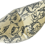 A close-up of a cream-colored fabric product, likely a pillow or cushion cover, featuring a black line art pattern of horses and wild horses.