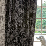 Black curtains with a white line-art illustration pattern of various figures and faces, hanging next to a window with a white dog statue in the foreground.