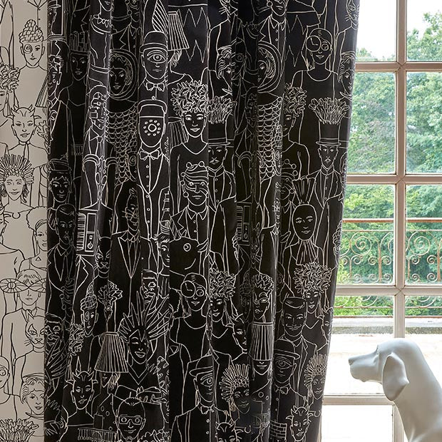 Black curtains with a white line-art illustration pattern of various figures and faces, hanging next to a window with a white dog statue in the foreground.