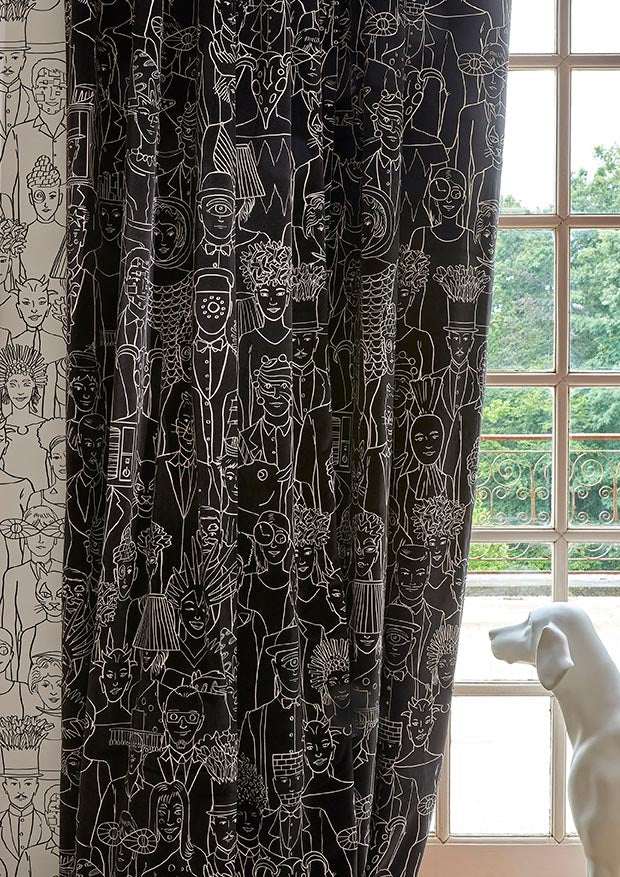 Black curtains with a white line-art illustration pattern of various figures and faces, hanging next to a window with a white dog statue in the foreground.
