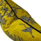 A close-up of a yellow fabric product, likely a pillow or cushion cover, featuring a gray crane and flowering tree branch pattern with black piping along the edge, set against a plain white background.