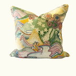 A square decorative throw pillow featuring a vibrant, multicolored abstract landscape pattern with mountains, waves, and flowers on a cream background.