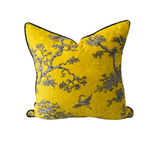 A square yellow velvet throw pillow with a gray and black toile-style print of trees and a crane, finished with black piped edges, shown on a plain white background.